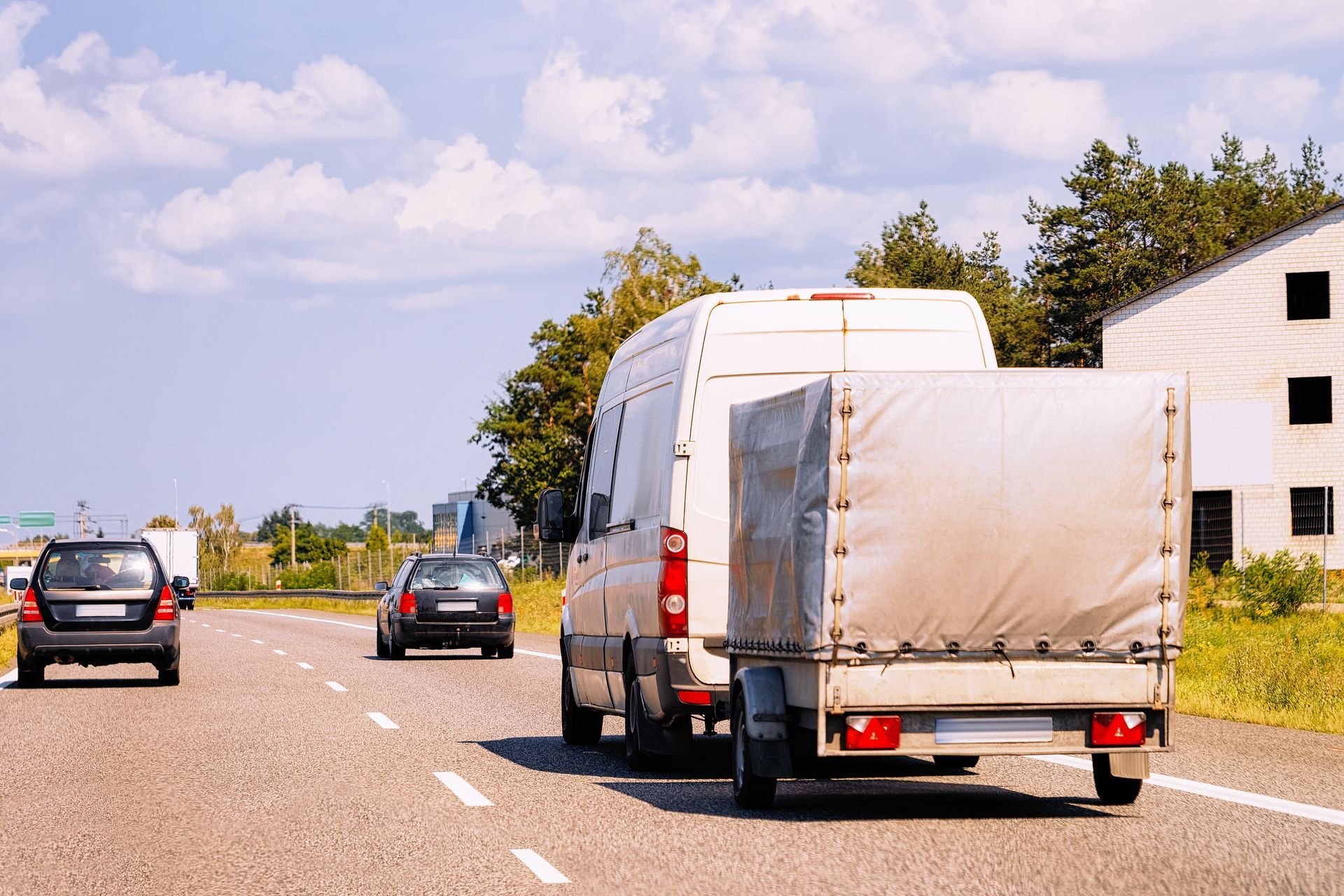 A white van with a trailer is driving down a highway.