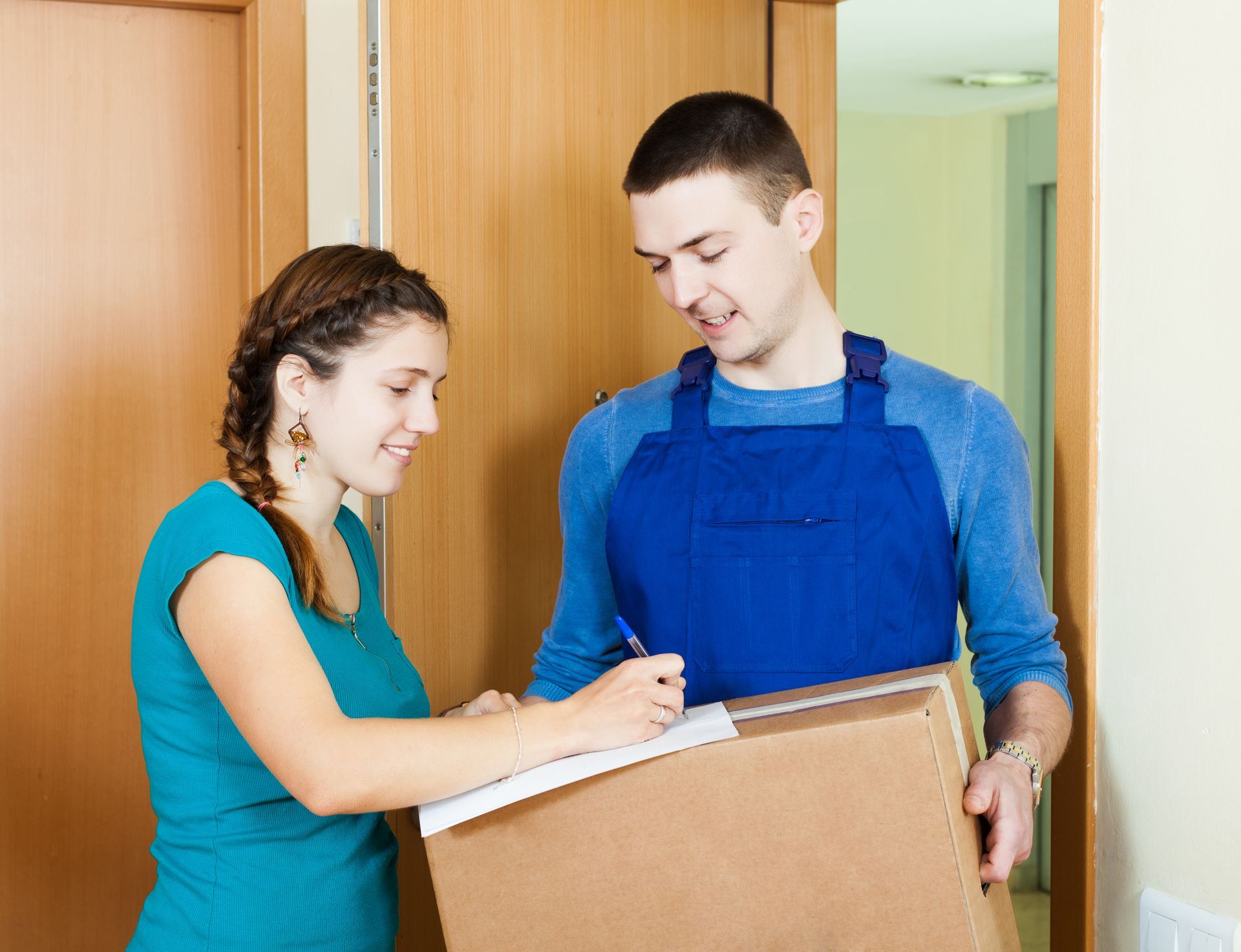 A man is holding a box and a woman is writing on a clipboard.