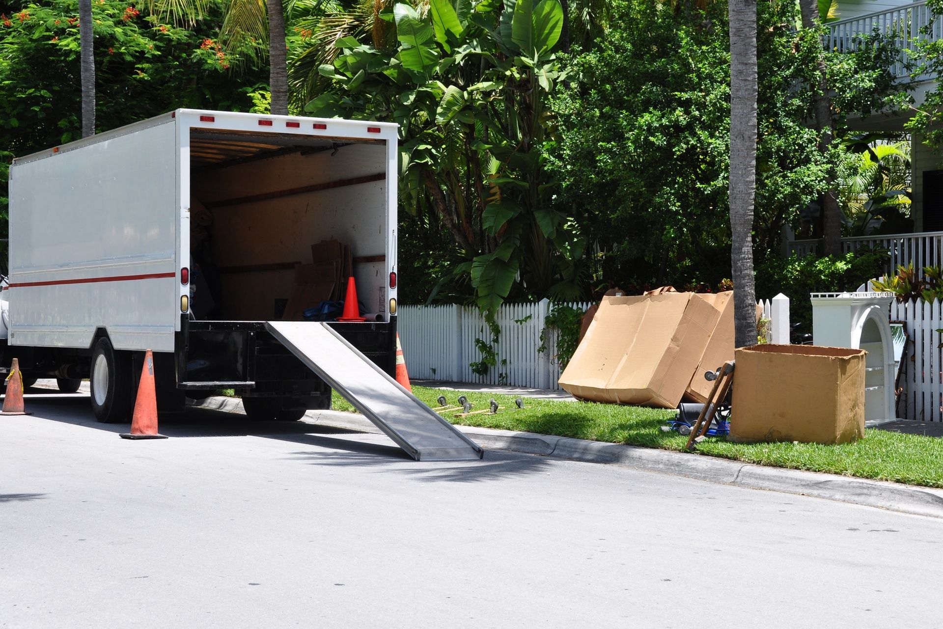 Moving truck parked on a street with ramp extended, cardboard boxes, and traffic cones.