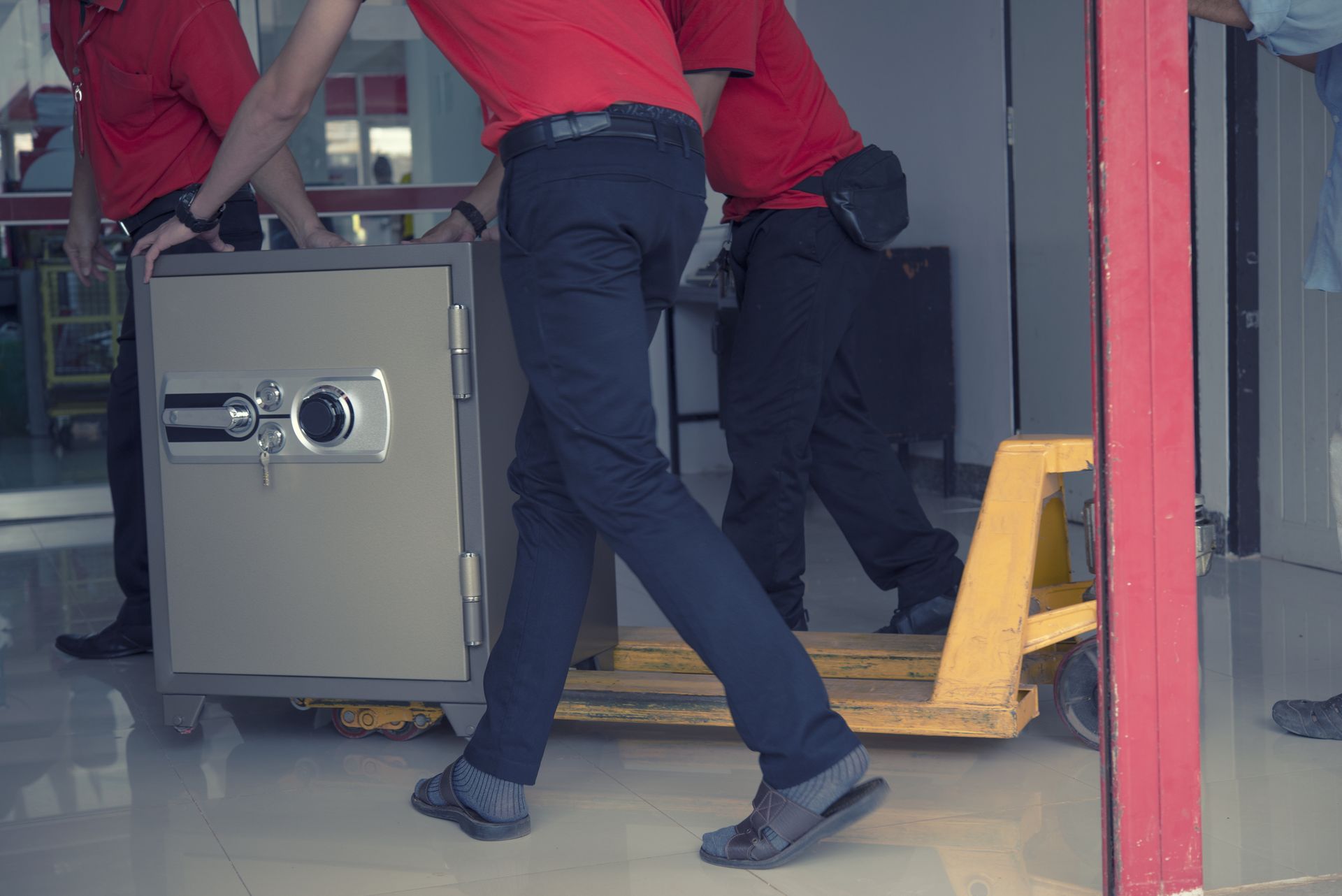 Men in red shirts moving a safe with a hand truck.