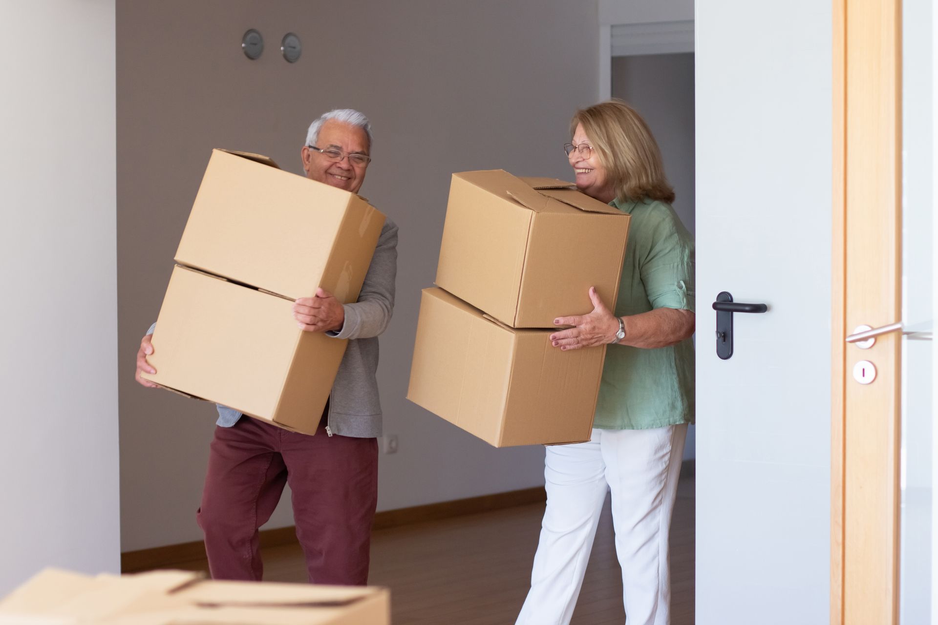 A man and a woman are carrying cardboard boxes into a room.