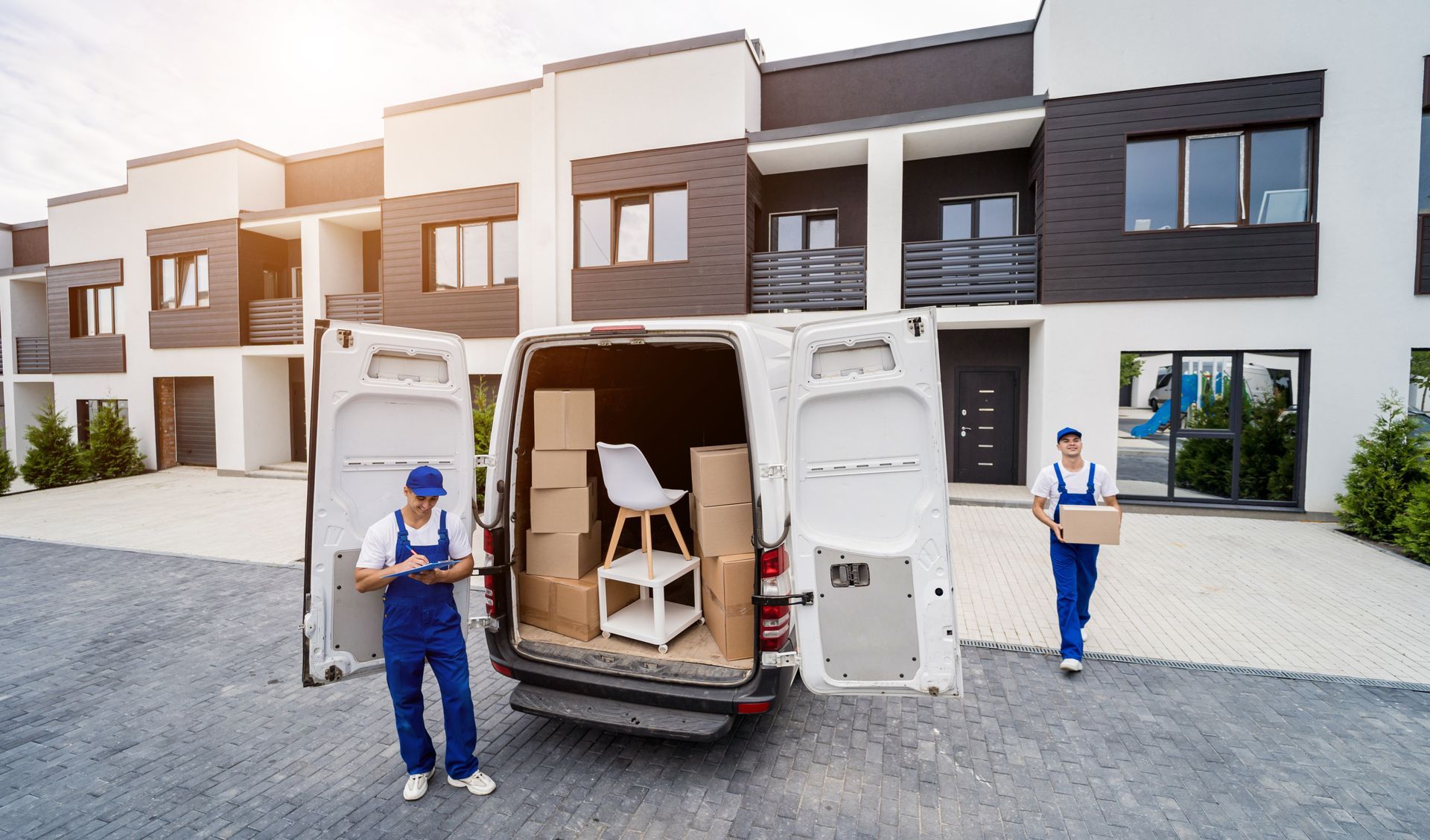 Two movers are loading a van with boxes in front of a house.