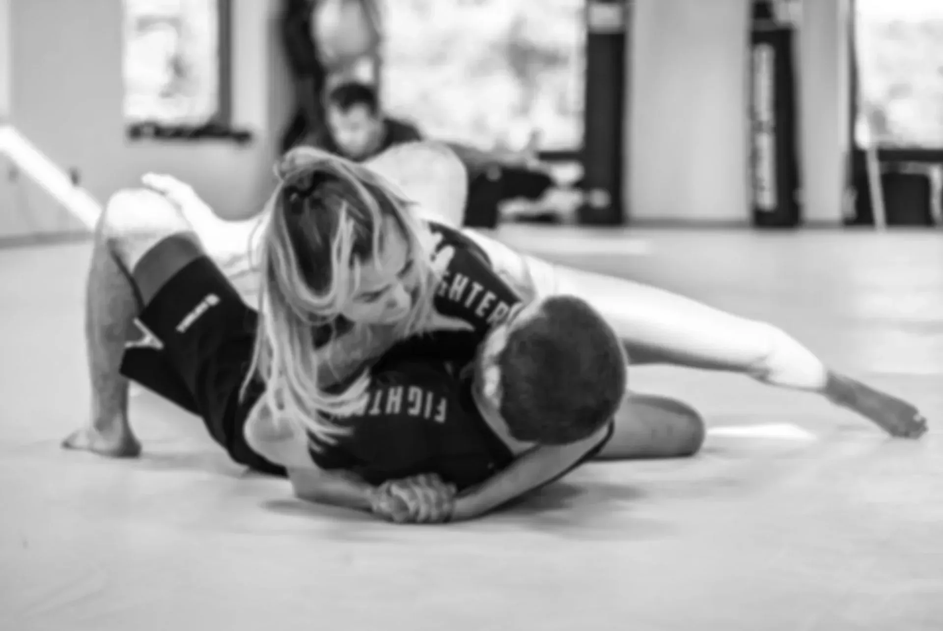 A man and a woman are wrestling on a mat in a gym.