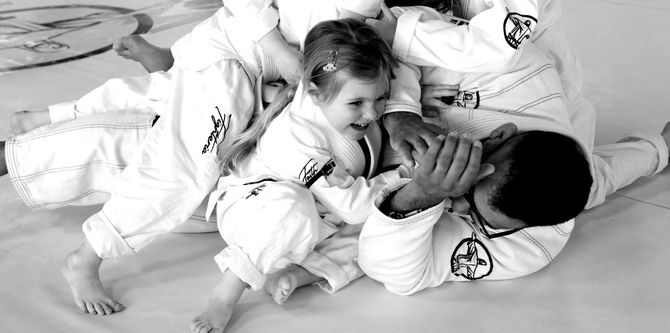 A man in a BJJ gi is teaching a group of children.