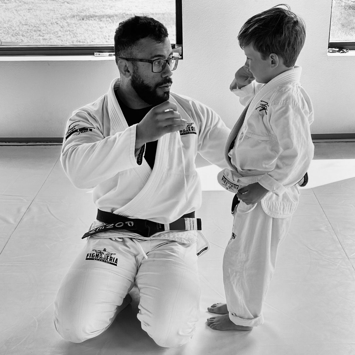 Two children practice Brazilian Jiu-Jitsu while other students watch.