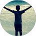 Silhouette of a person with arms outstretched on a beach, facing the ocean.