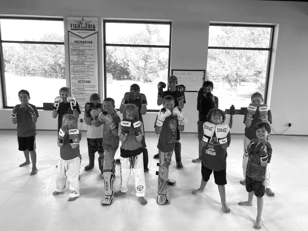 A group of young boys wearing boxing gloves are posing for a picture in a gym.