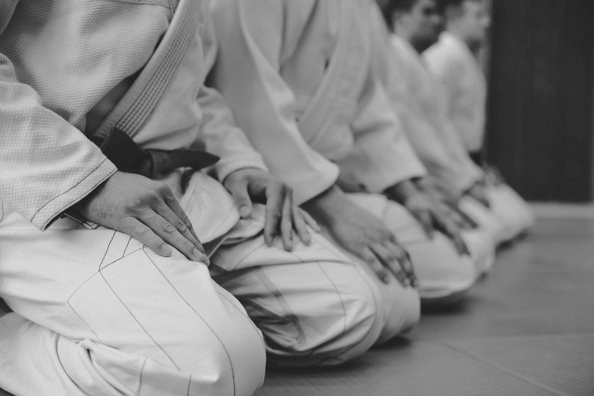 A row of martial artists in white uniforms kneeling in traditional seiza posture on a studio floor.