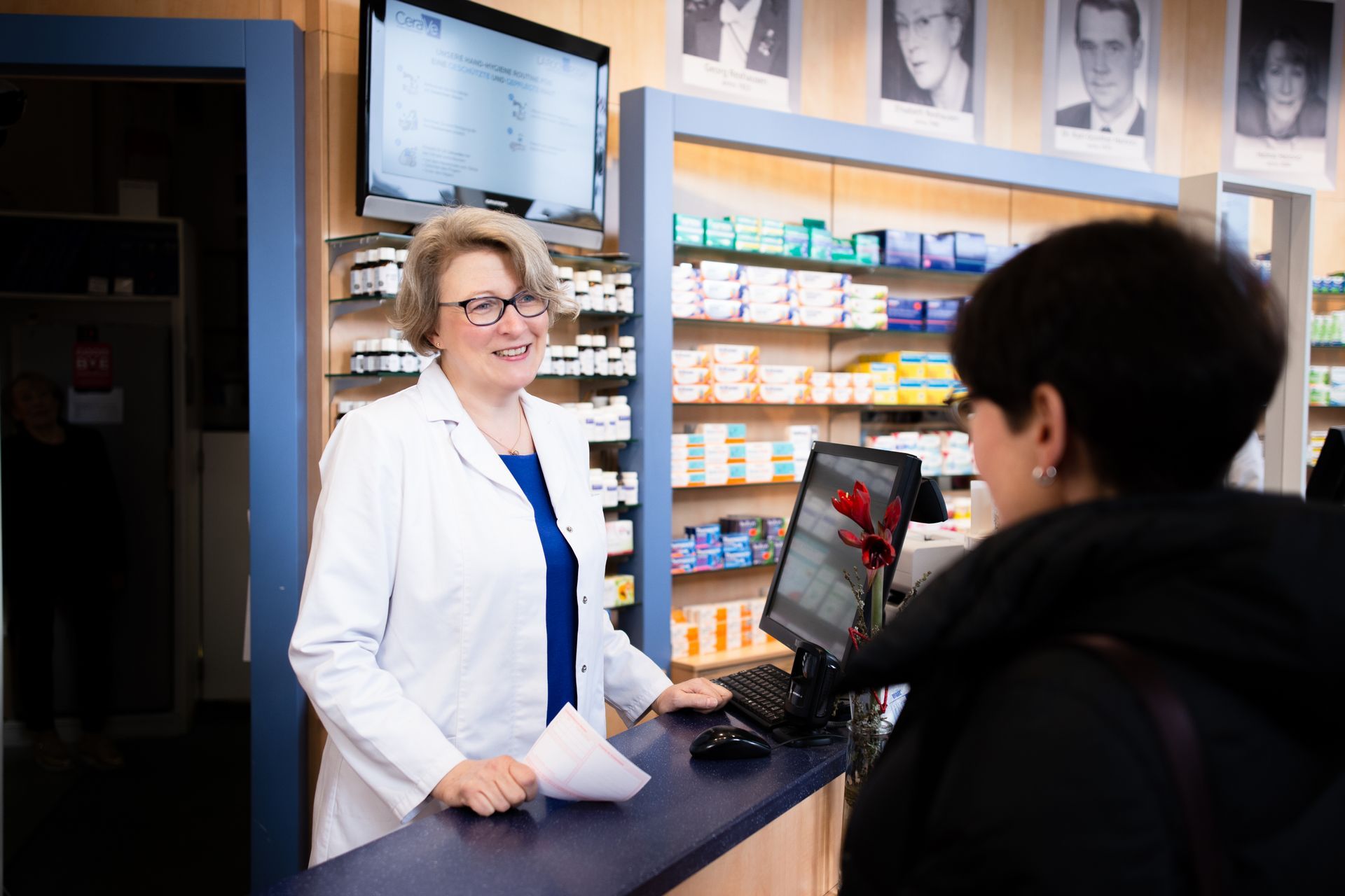 Eine Frau steht an einem Tresen in einer Apotheke und spricht mit einem Kunden.