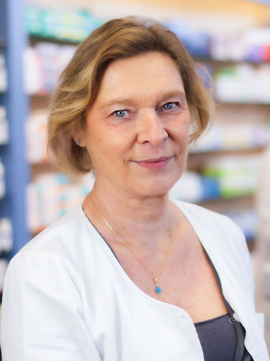 Eine Frau trägt in einer Apotheke eine weiße Jacke und eine Halskette.