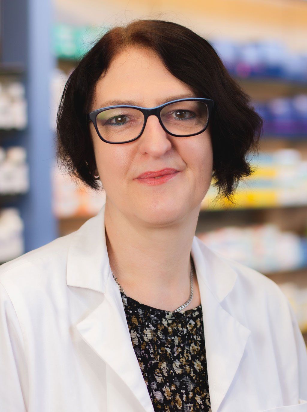 Eine Frau mit Brille und weißem Kittel steht in einer Apotheke.