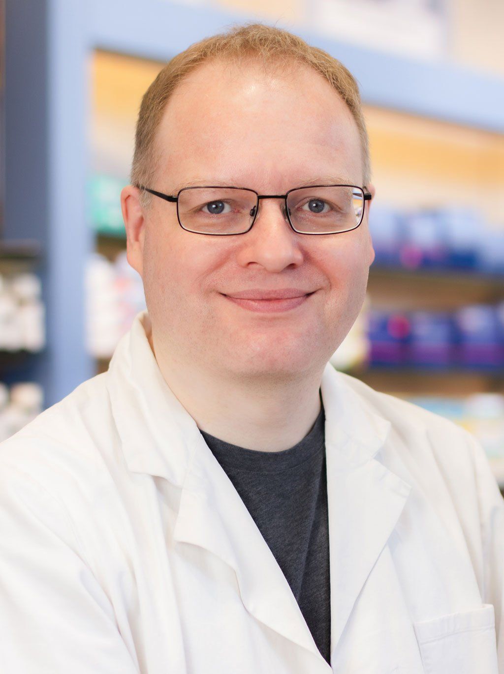 Ein Mann mit Brille und weißem Laborkittel lächelt in die Kamera