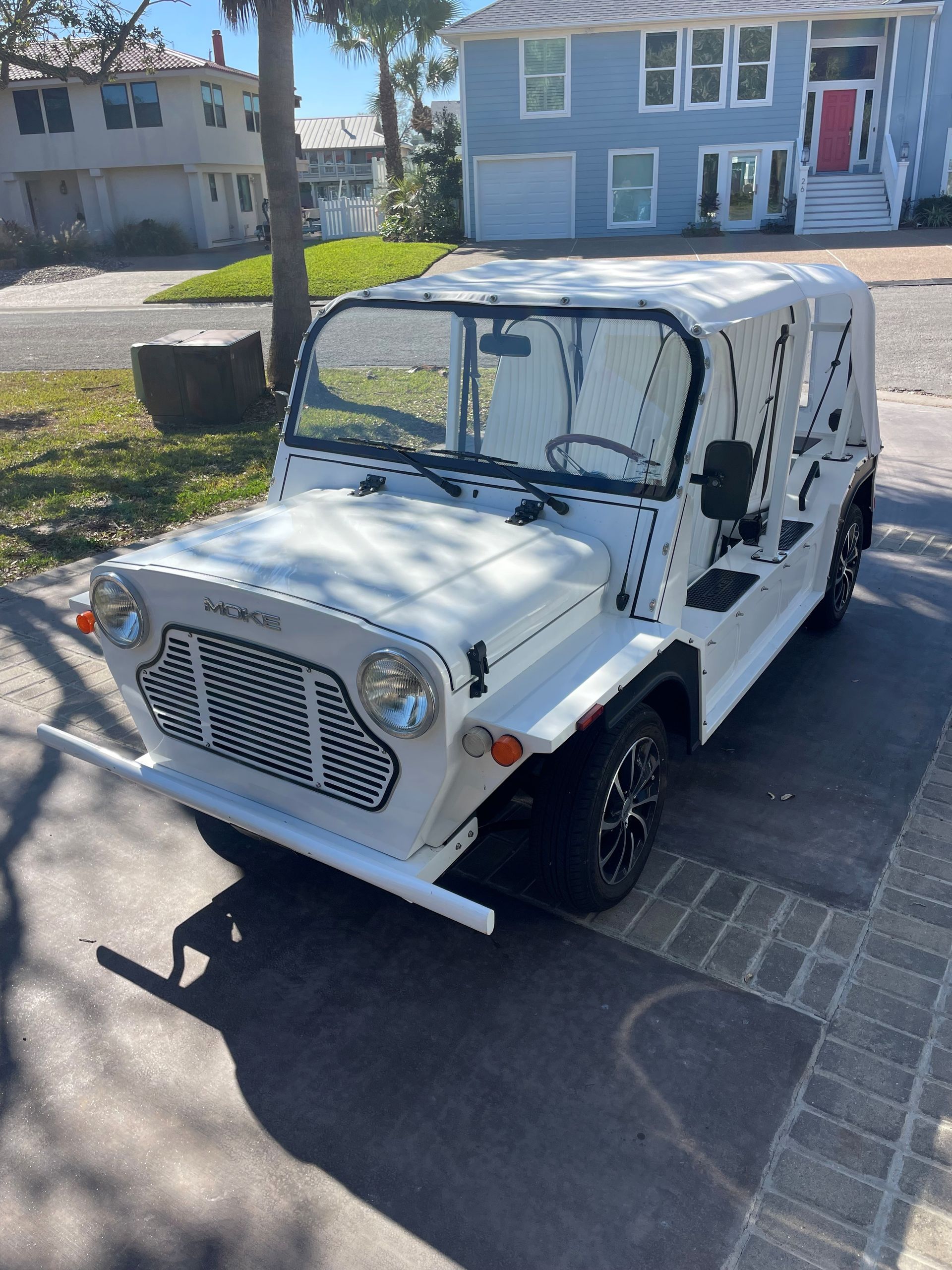 White Moke-style vehicle with a white top and black wheels parked on a paved driveway in front of a house.