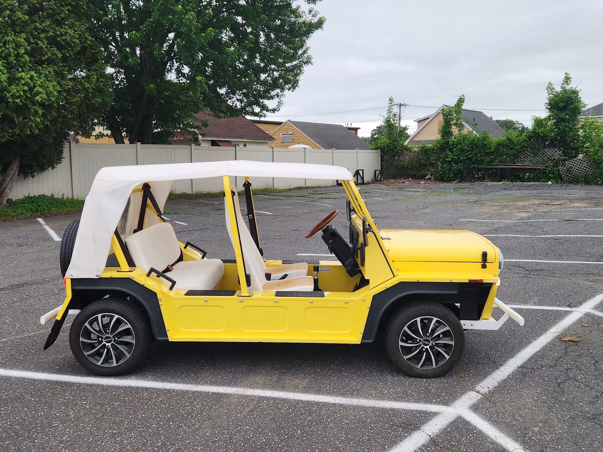 Yellow open-top car with white seats and canopy parked on asphalt.