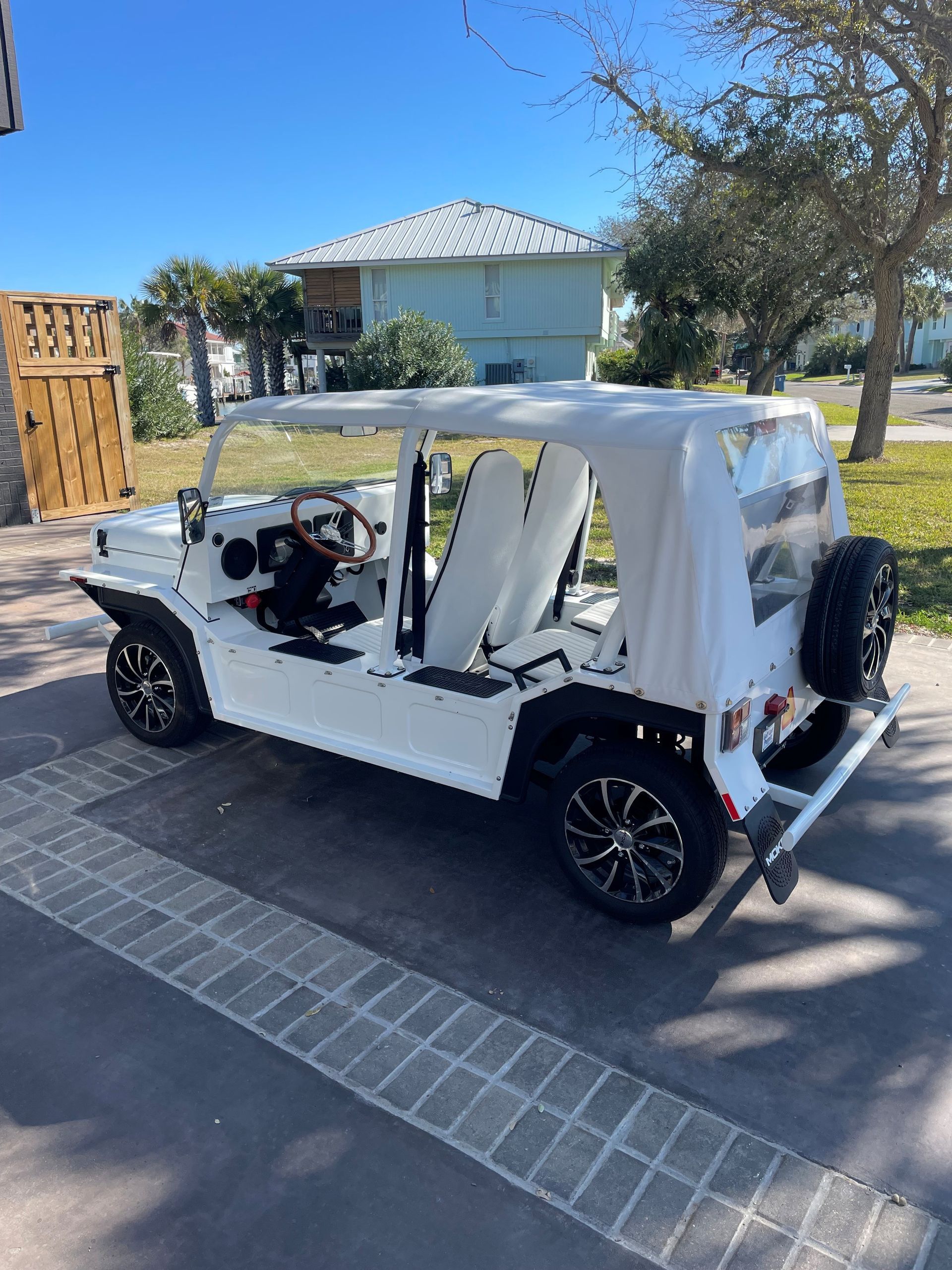 White Moke-style vehicle with a white top and black wheels parked on a paved driveway in front of a house.