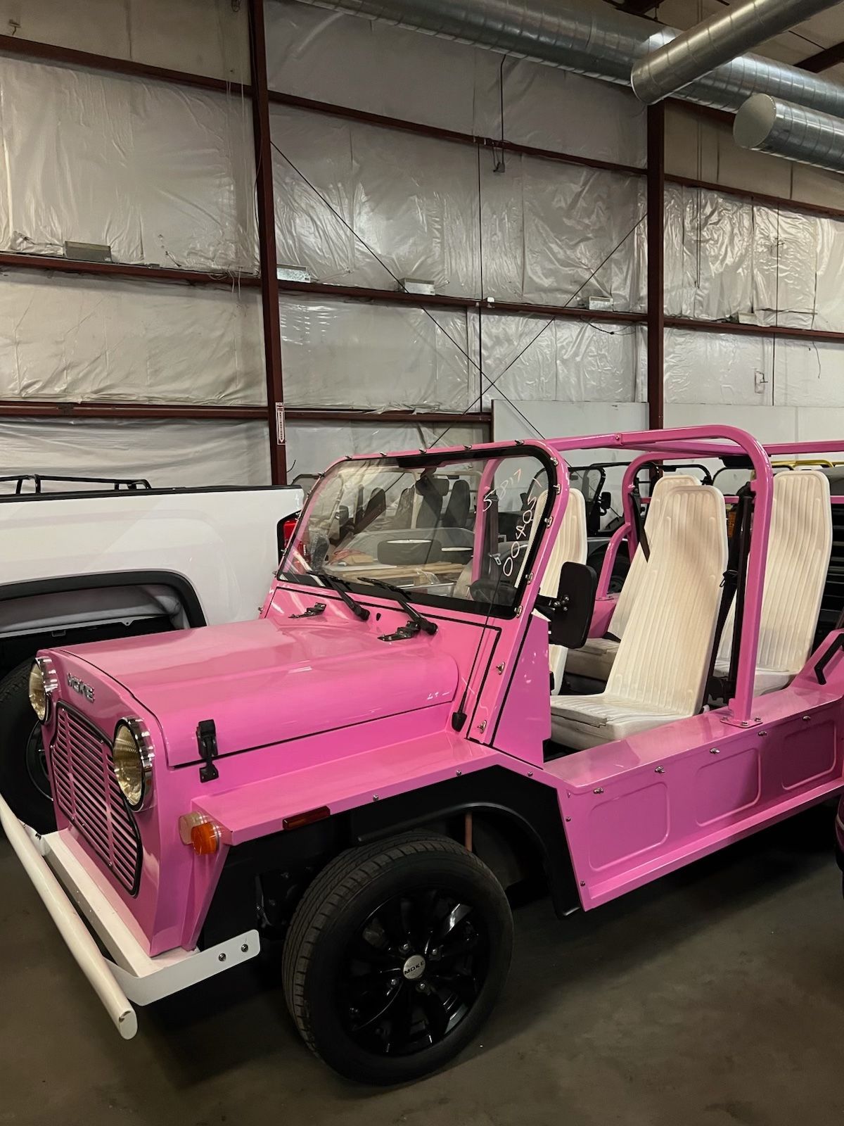 Pink, open-top vehicle with white seats, black wheels, and white bumper parked inside a warehouse.