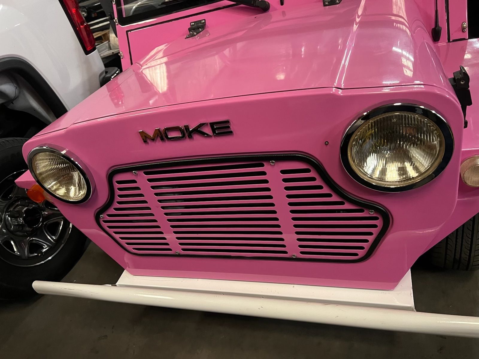 Pink, open-top vehicle with white seats, black wheels, and white bumper parked inside a warehouse.