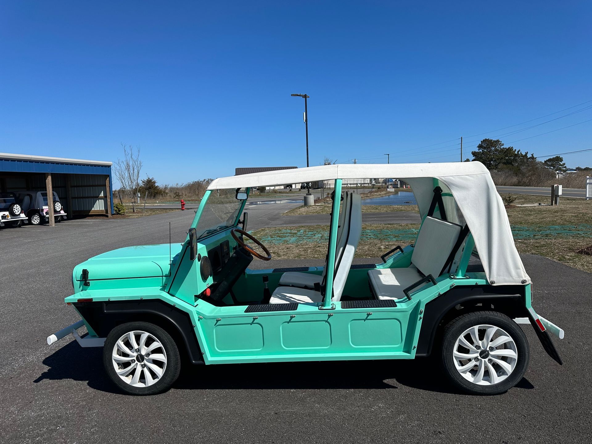 Mint-green open-top electric vehicle with white roof and wheels, parked outdoors on a sunny day.