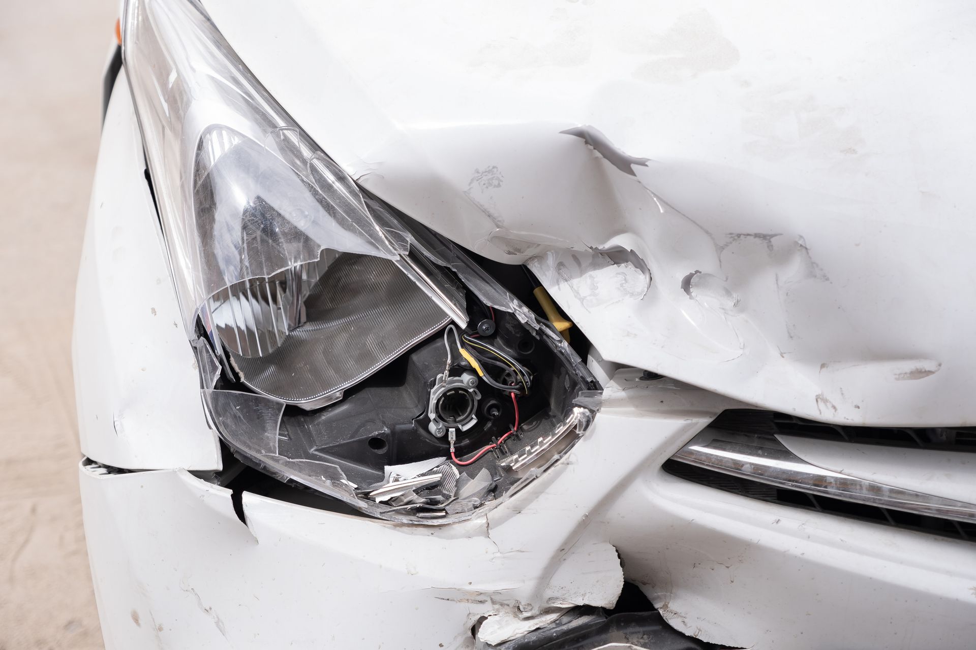 A close up of a white car with a damaged headlight.