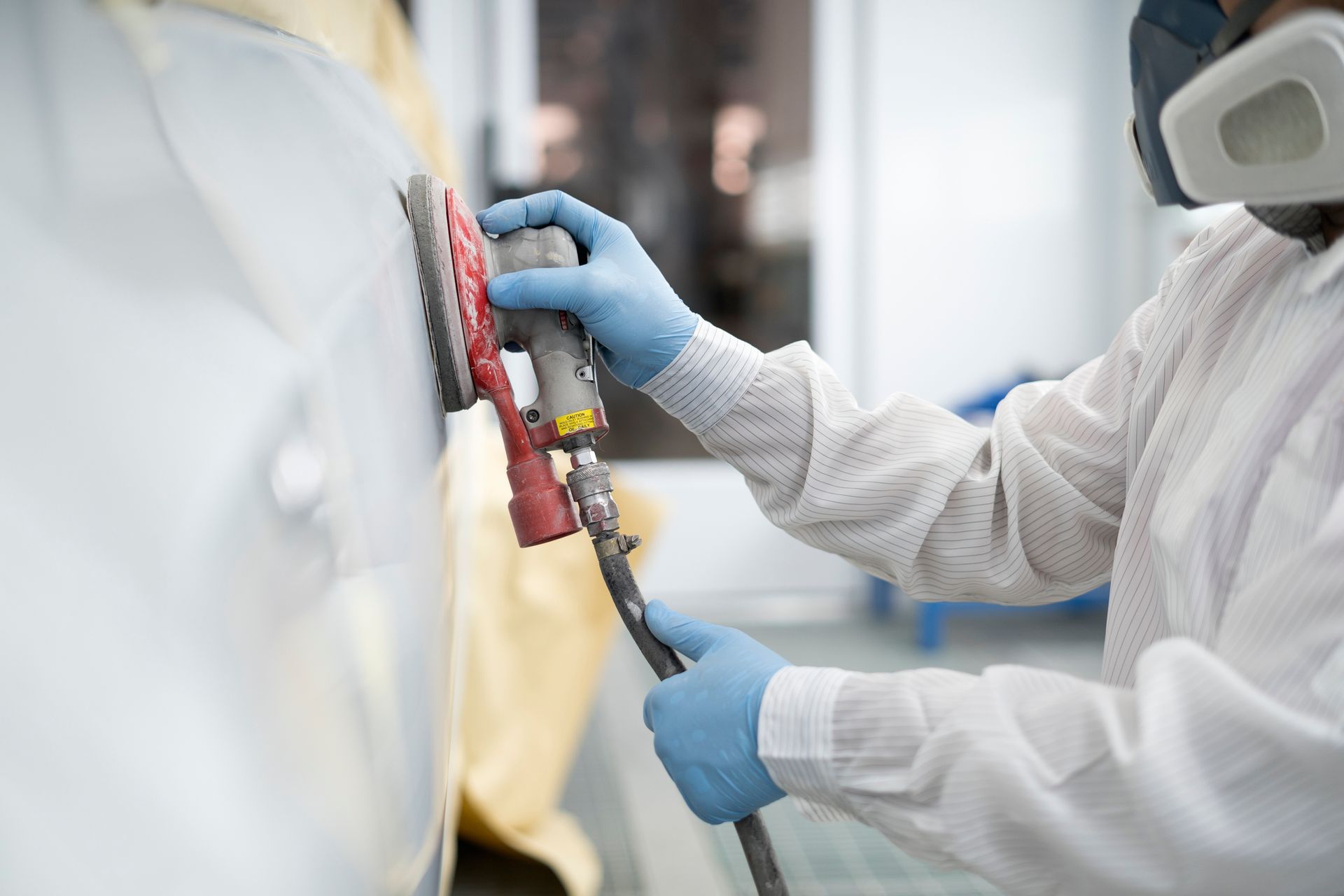 A man wearing a mask and gloves is sanding a car.