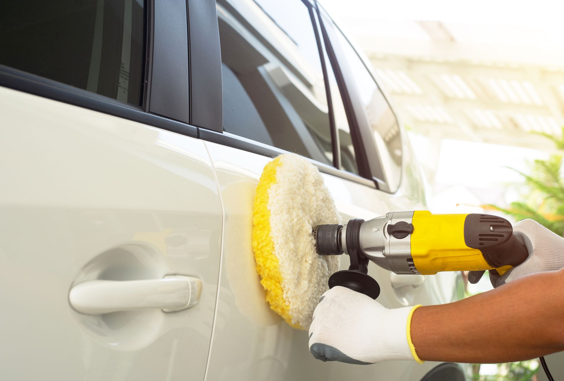 A person is polishing a white car with a yellow polisher.