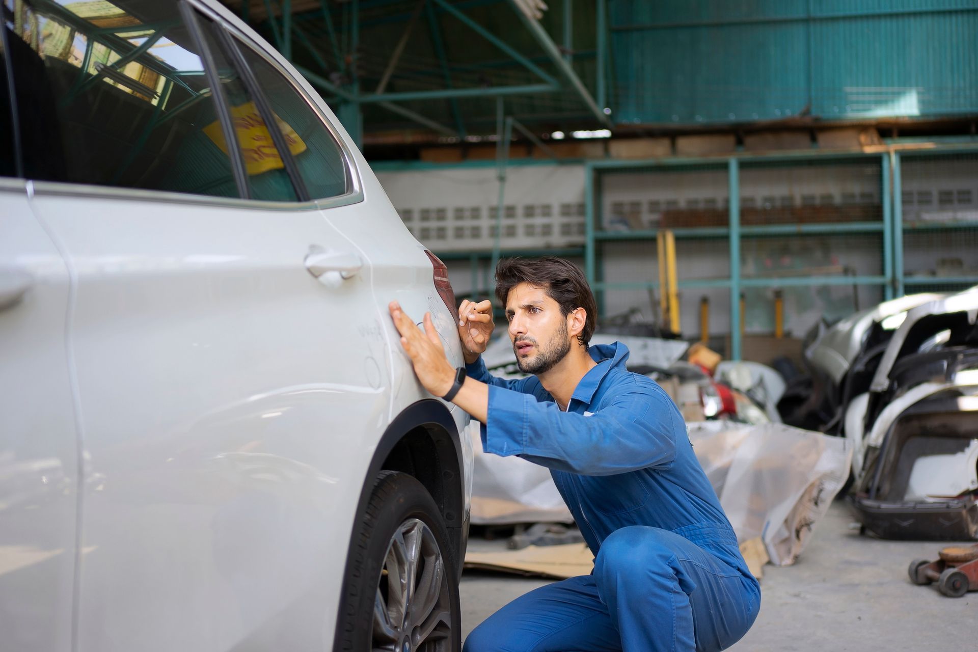 A man is kneeling down next to a white car in a garage.