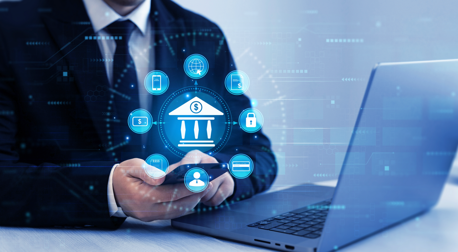 A man in a suit and tie is using a laptop and a cell phone.