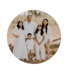 Family of four in white outfits standing together outdoors in a dry field.