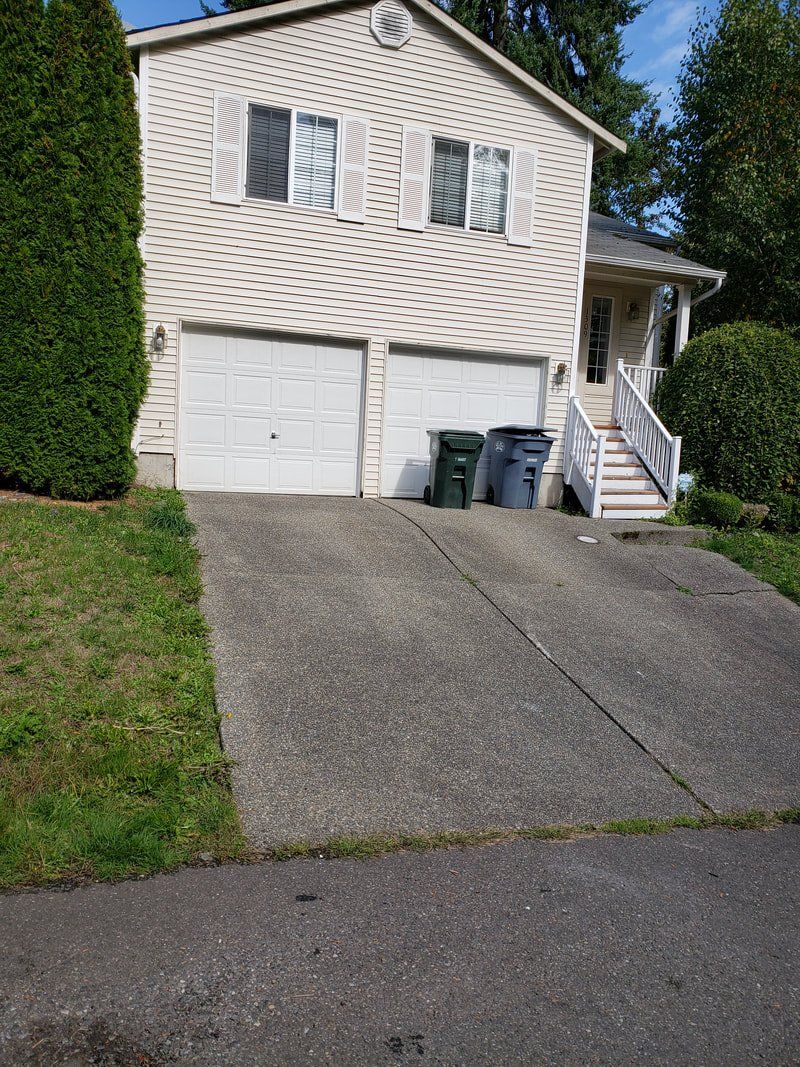 A white house with two garage doors and a driveway leading to it.