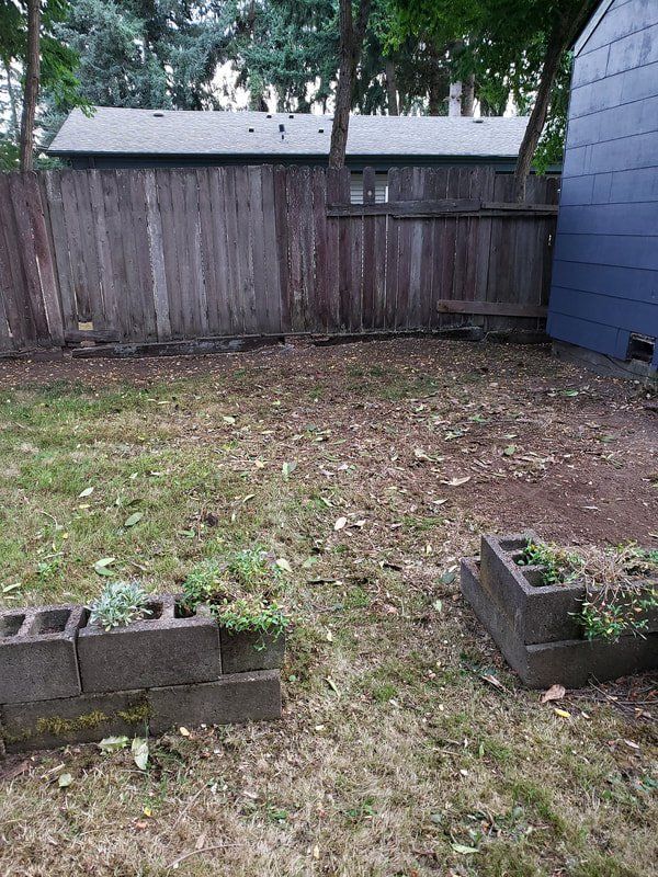 A backyard with a wooden fence and concrete blocks in the grass.