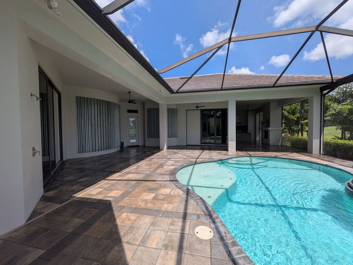 Patio with pool under a screened enclosure. Paved flooring, white walls, and blue pool water.