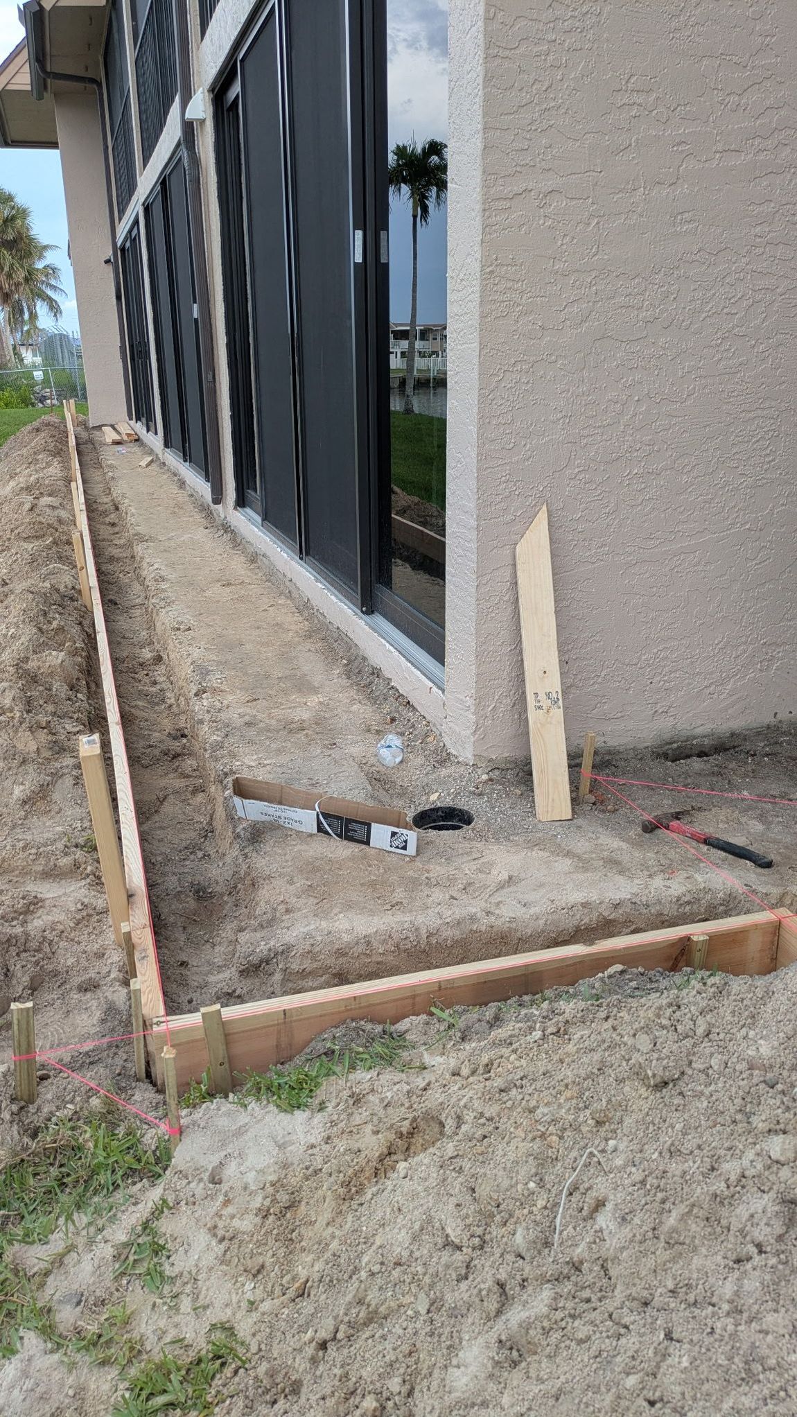 Construction site with wooden forms for a concrete walkway next to a building with windows.
