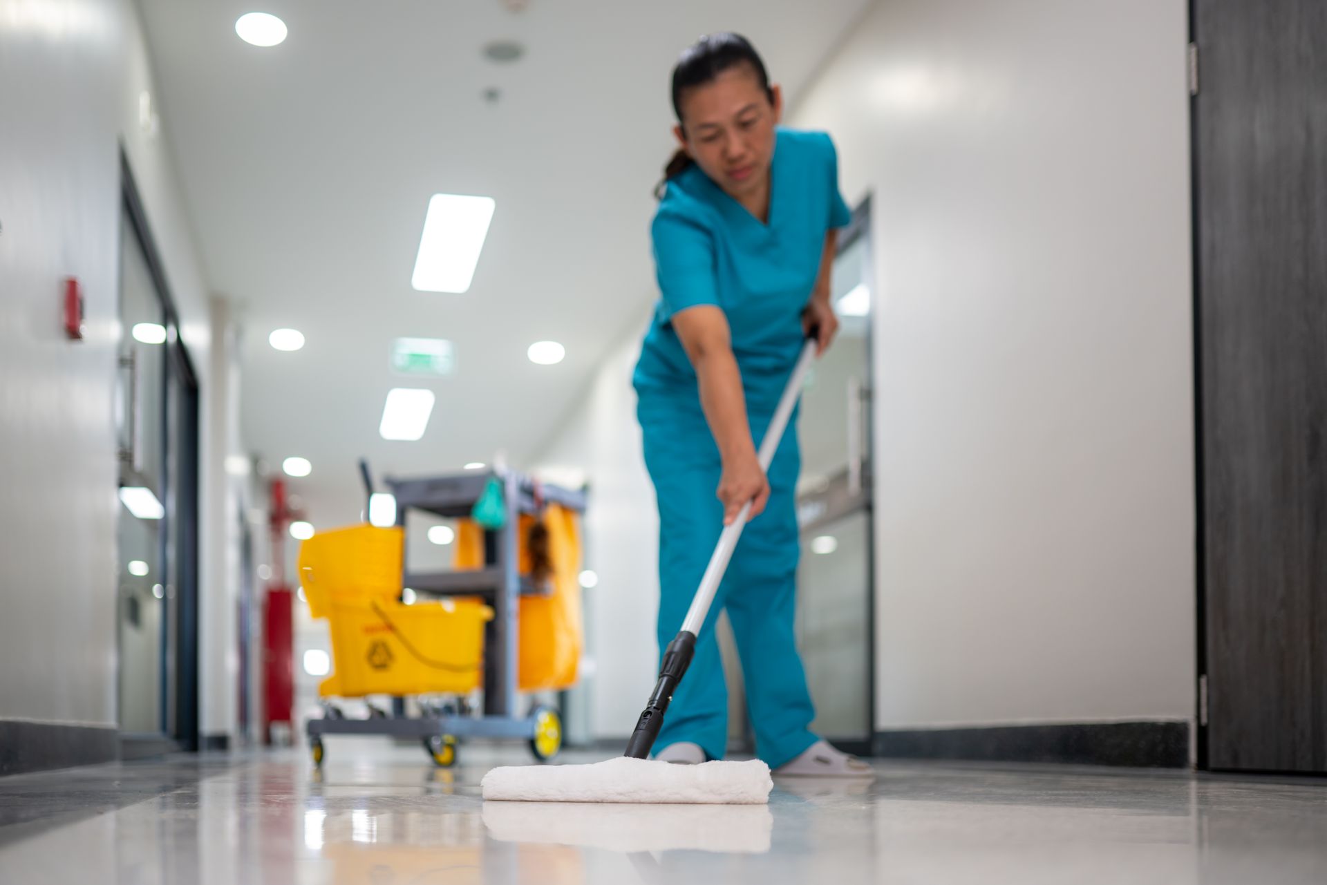 A nurse is cleaning the floor of a hospital with a mop.