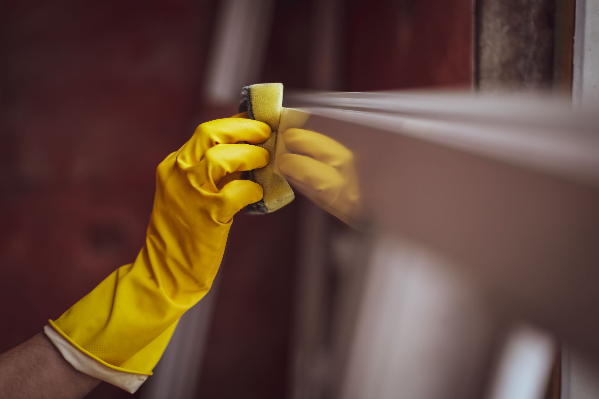 A person wearing yellow gloves is cleaning a window with a sponge.