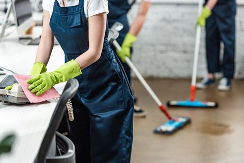 A woman in green gloves is cleaning a desk in an office.