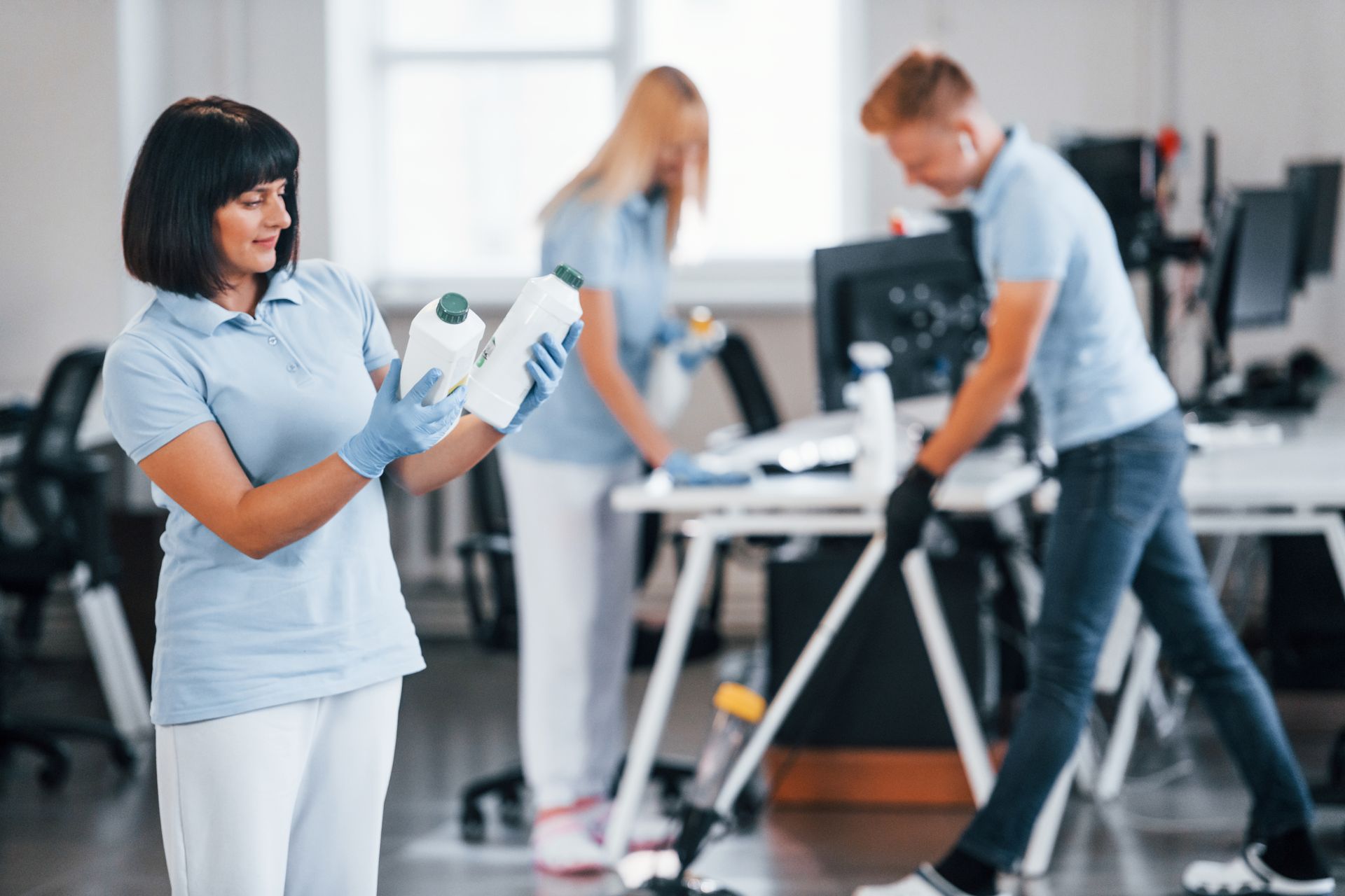 A woman is holding a bottle of detergent in an office.