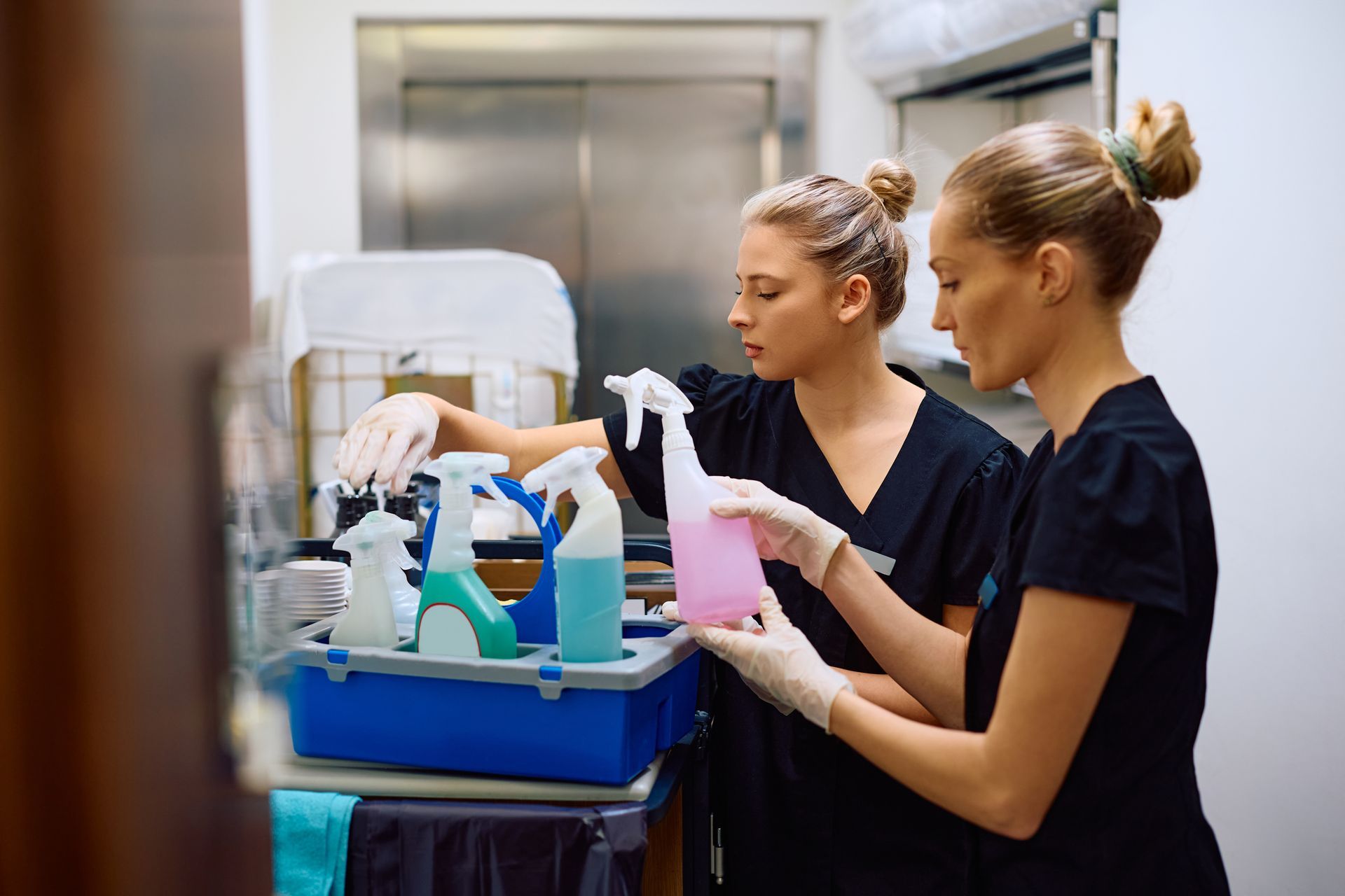 Two women are cleaning a room with cleaning supplies.