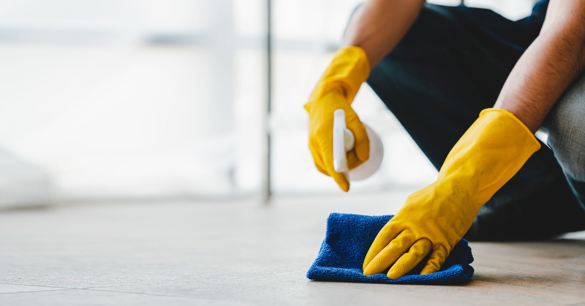 A person wearing yellow gloves is cleaning the floor with a cloth.