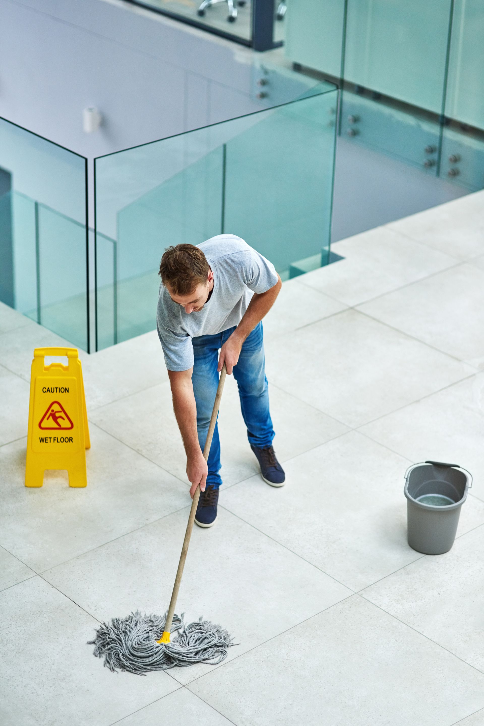 A man is mopping the floor of a building next to a caution sign.