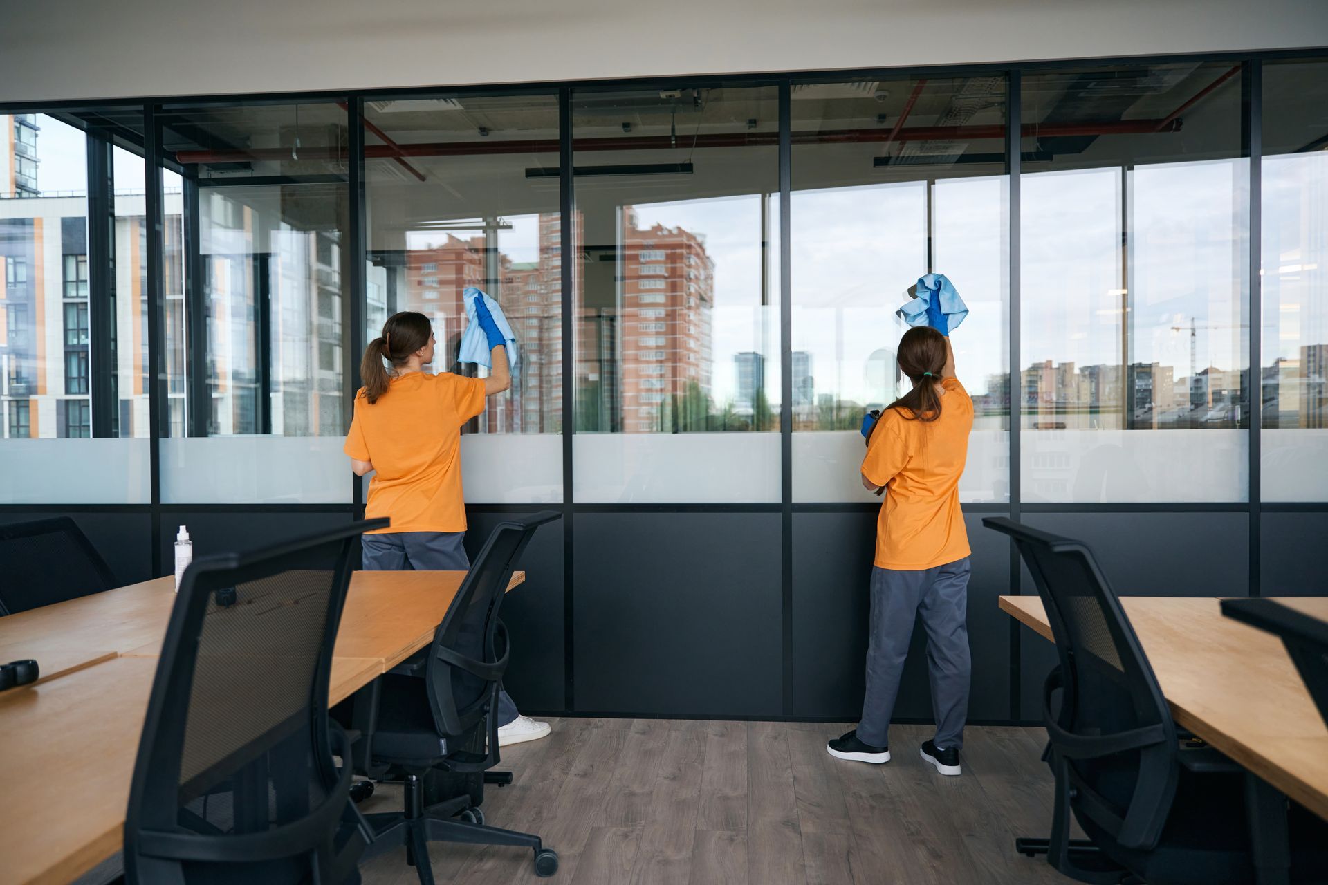 Two women are cleaning windows in an office.