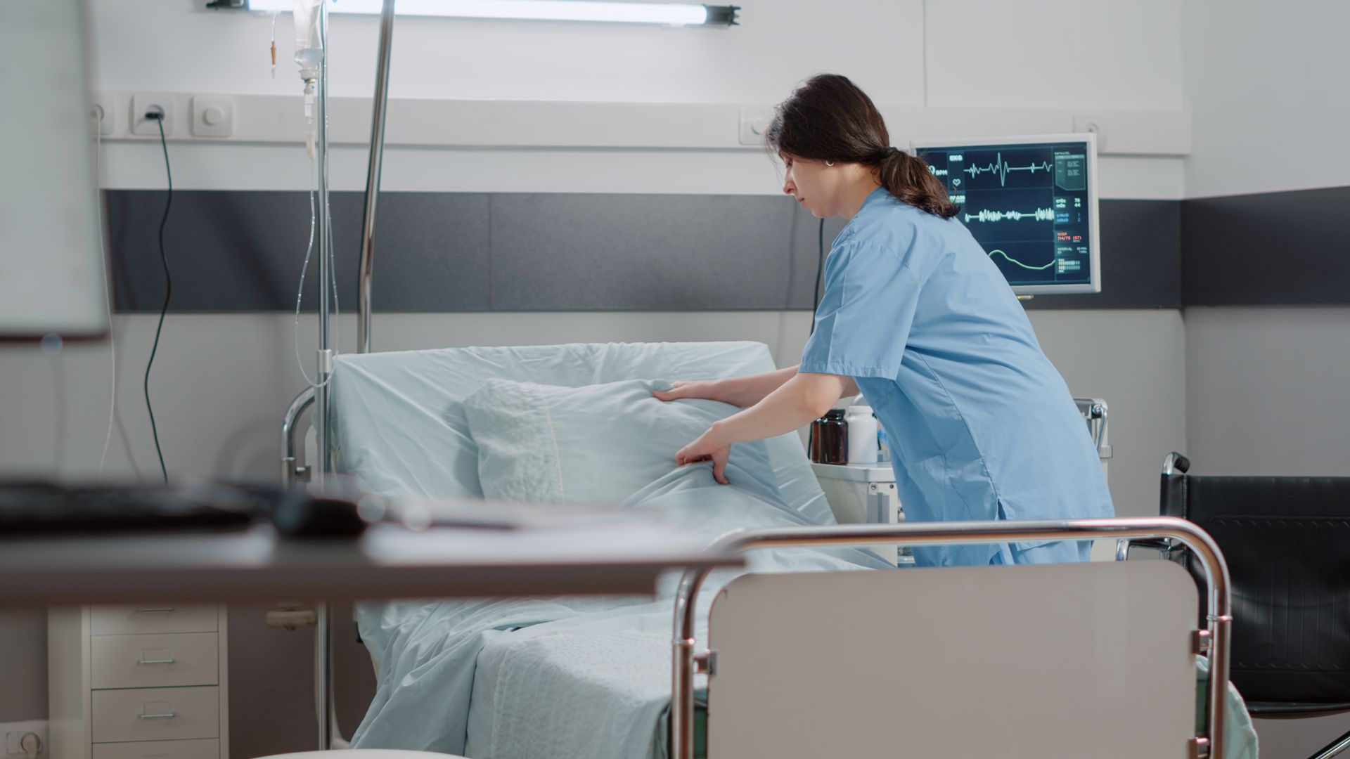 A nurse is making a bed in a hospital room.