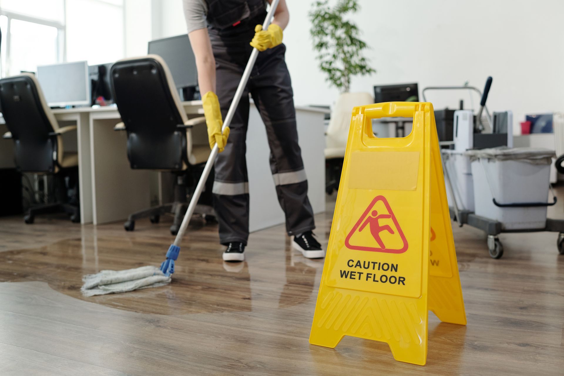 A man is mopping the floor in an office next to a caution sign.