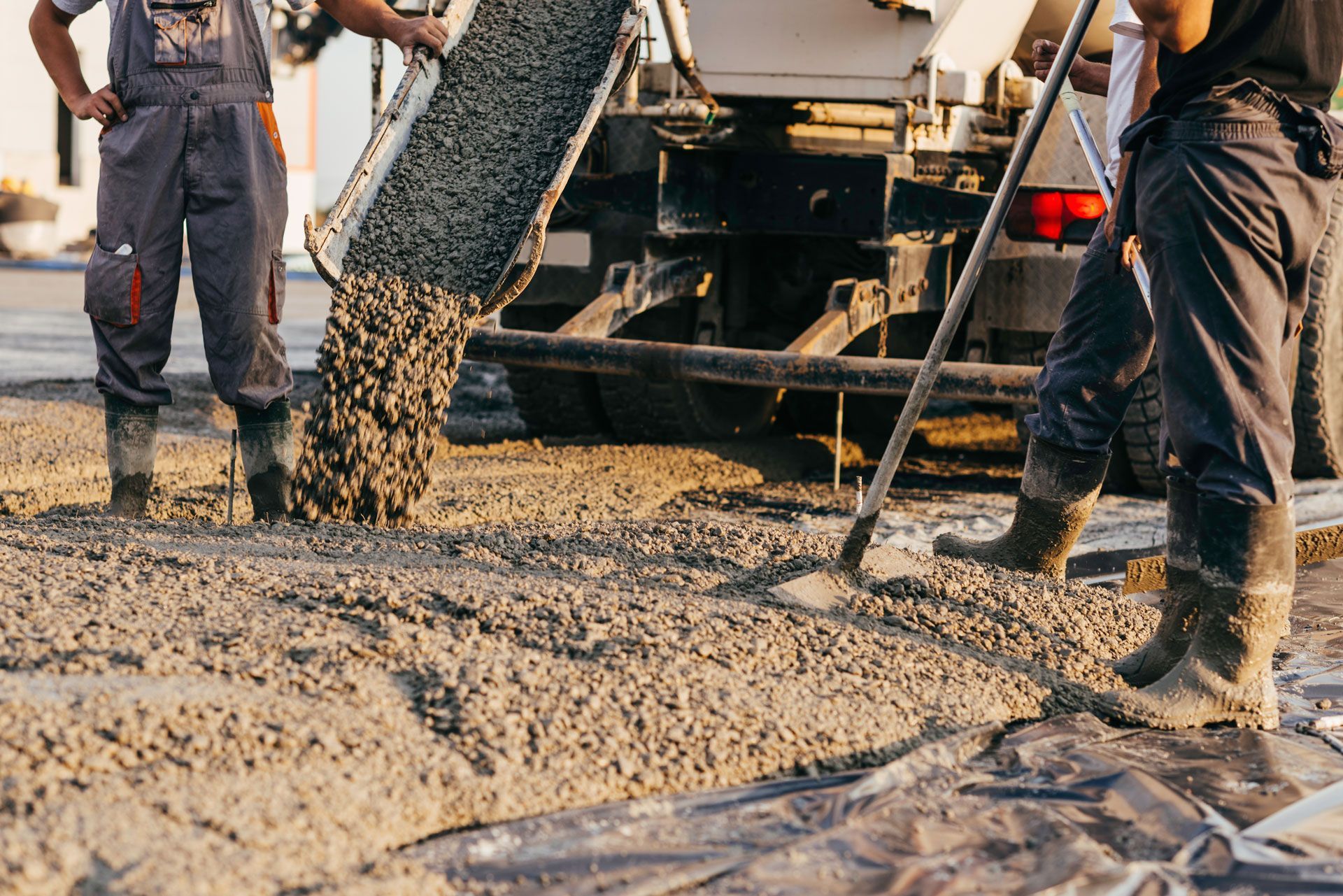 Concrete being poured from a truck onto a surface, two workers are present.
