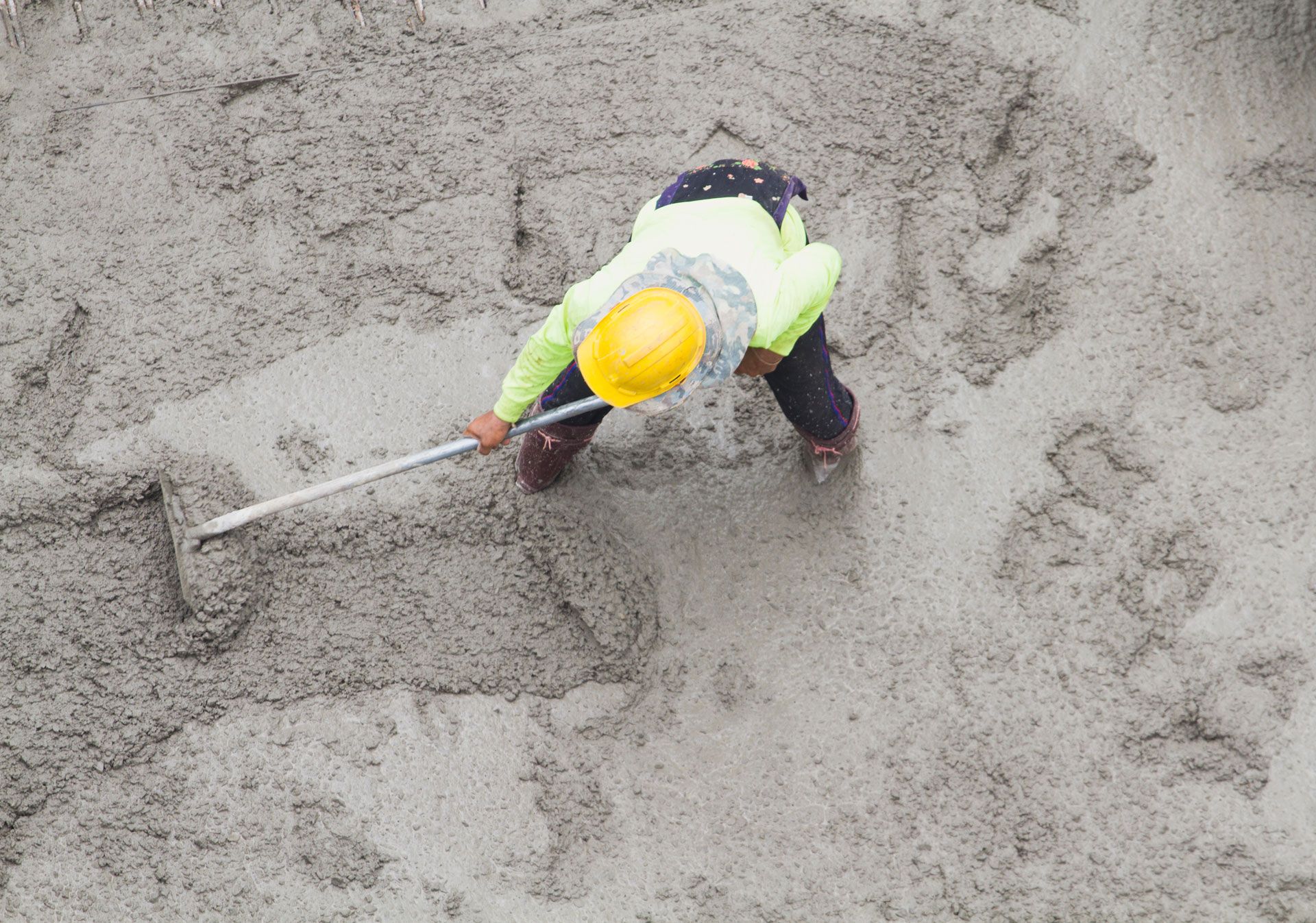 Person in safety vest and helmet raking wet cement.