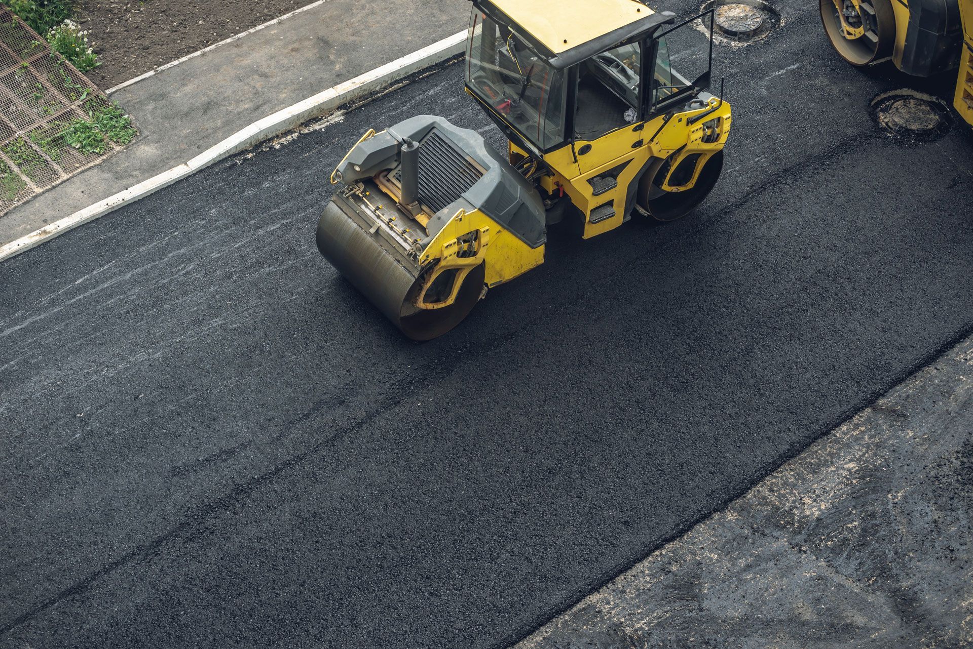 Yellow road roller paving fresh black asphalt on a street