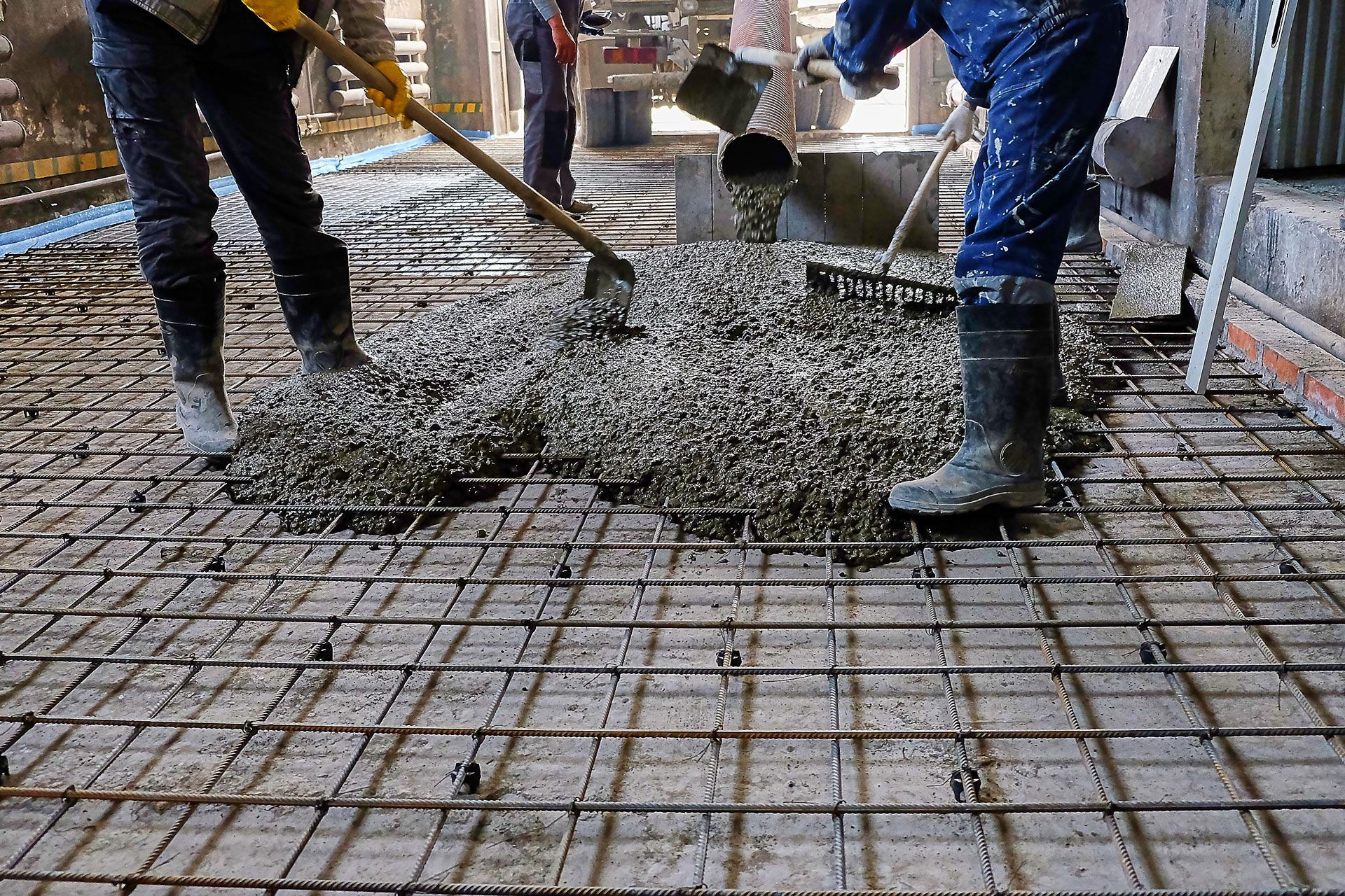 Workers pouring and spreading concrete over a rebar grid during construction.