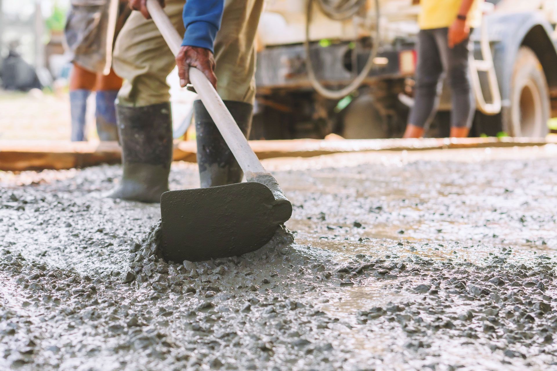 Worker smoothing wet concrete with a large trowel; construction site.