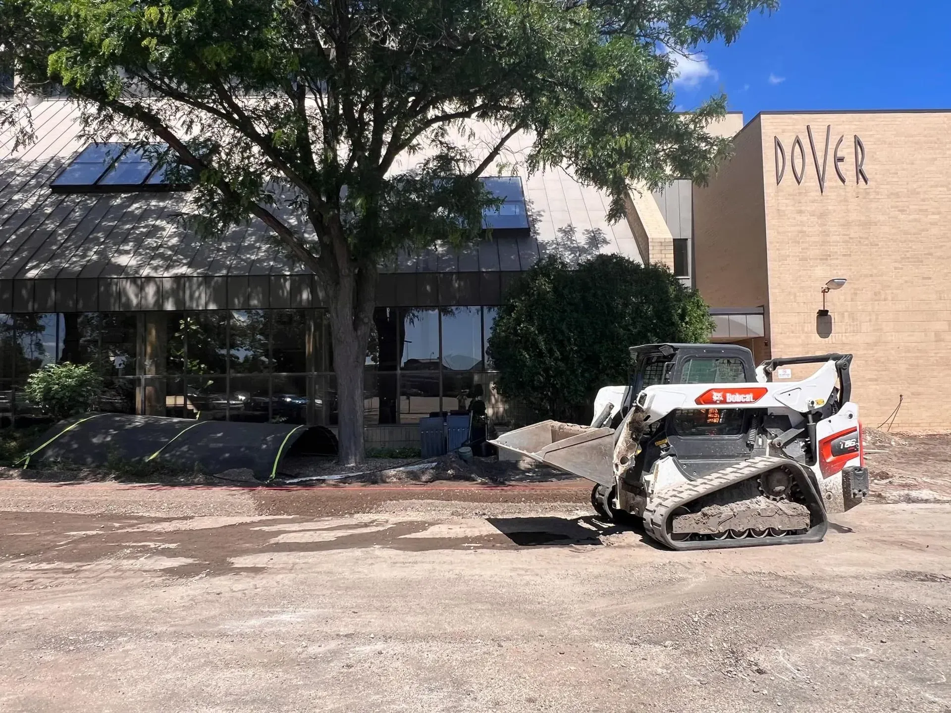 A white Bobcat skid steer on a construction site near a brick building with the word 