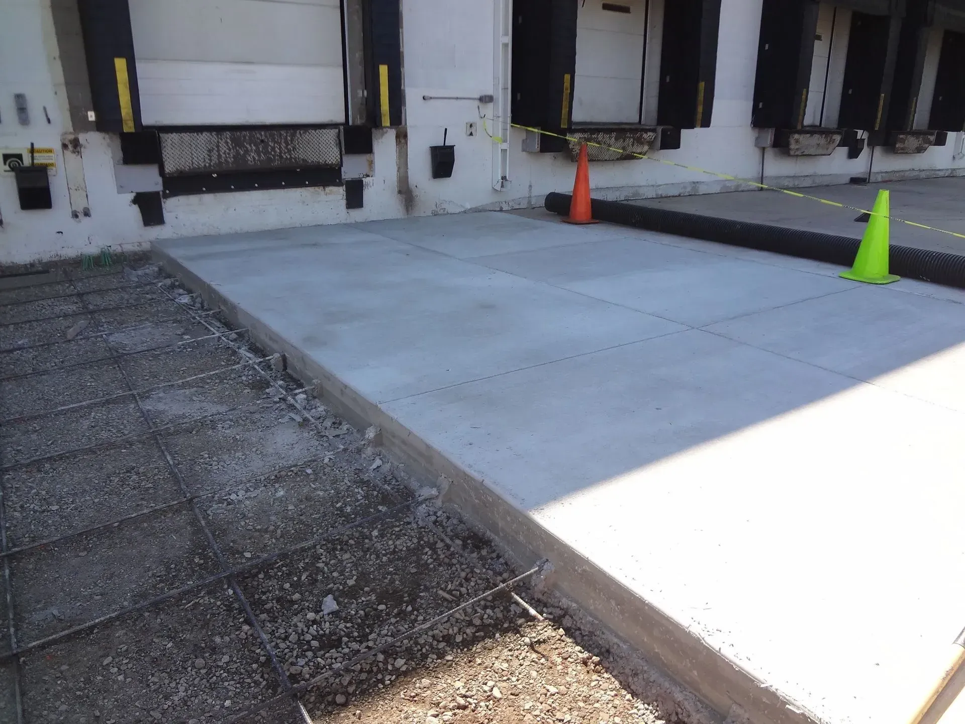 Concrete work in progress; new concrete laid in front of loading docks, with a rebar grid and traffic cones.