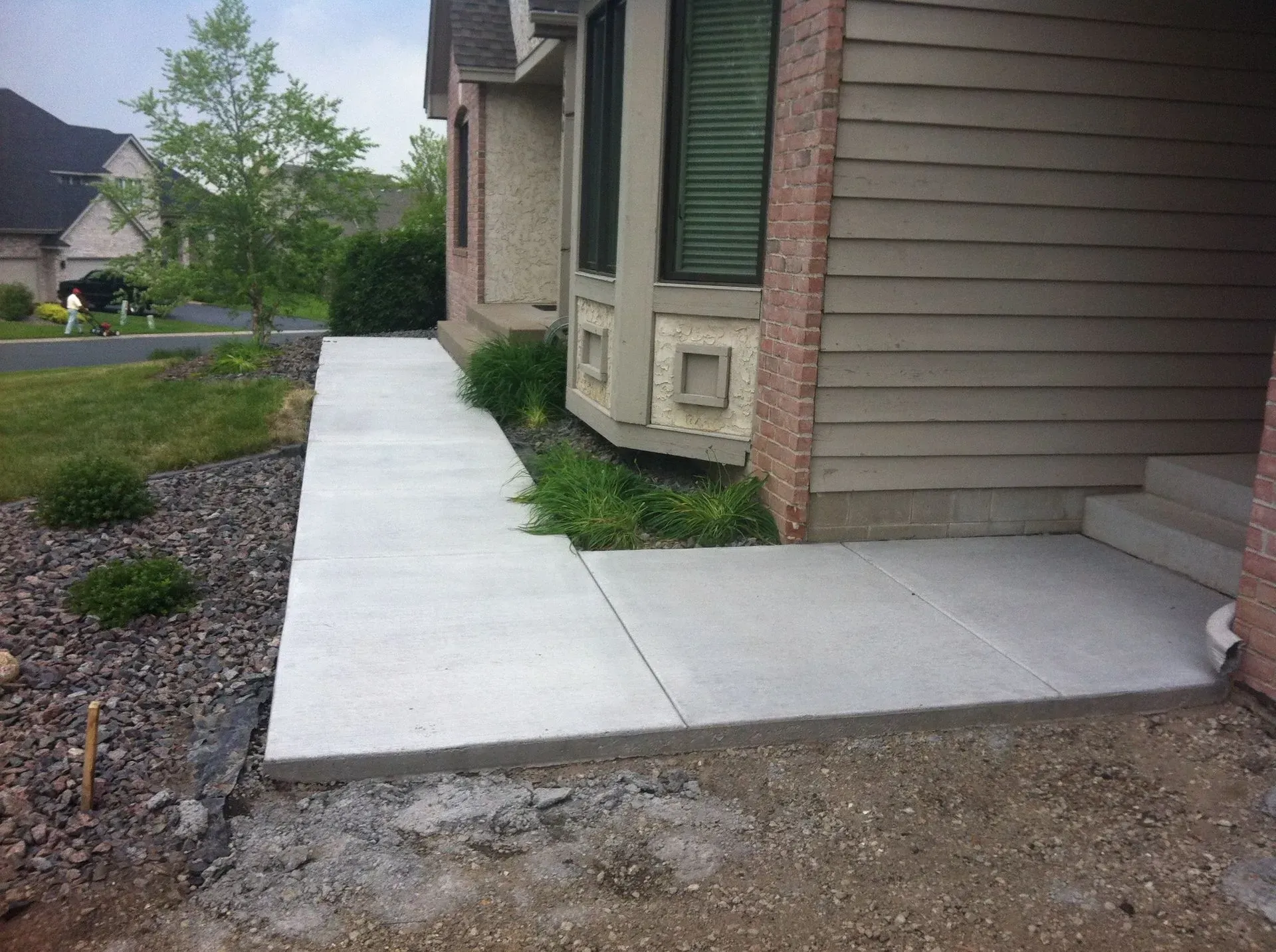 Concrete walkway leading to a house with tan siding, bay window, and grassy landscaping.
